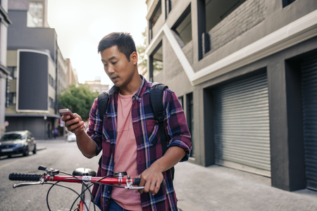 Young Asian man walking with his bike using a cellphoneの写真素材