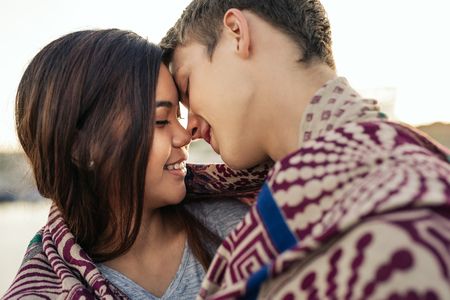 Young couple kissing while wrapped in a blanket together outsideの写真素材