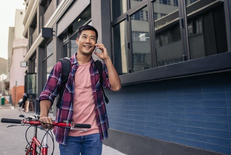 Smiling man walking with his bike talking on a cellphoneの写真素材