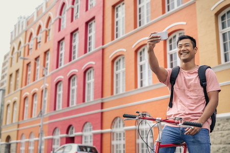 Smiling young man sitting on his bike taking a selfieの写真素材