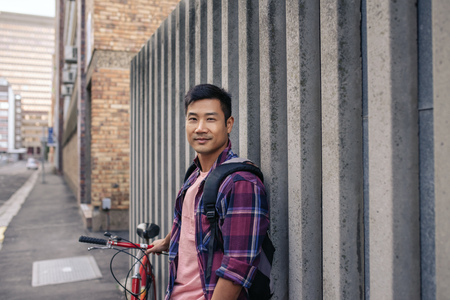 Smiling young man leaning against a wall with his bikeの写真素材