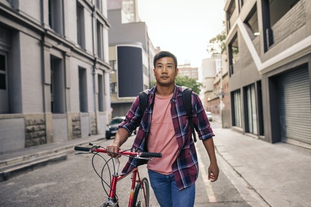 Young Asian man walking with his bike through city streetsの写真素材