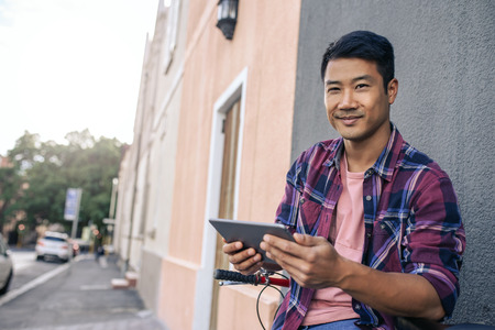 Smiling young man sitting on his bike using a tabletの写真素材