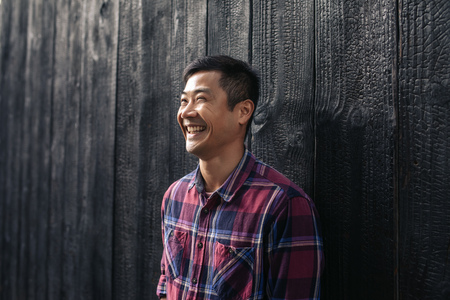 Laughing Asian man leaning against a wall in the cityの写真素材