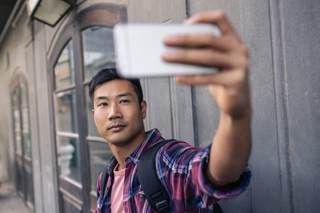 Confident young Asian man taking selfies on a city streetの写真素材