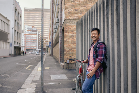 Smiling young man leaning with his bike against a wallの写真素材
