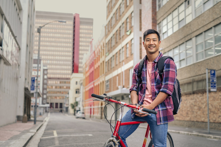 Smiling young man sitting on his bike in the cityの写真素材