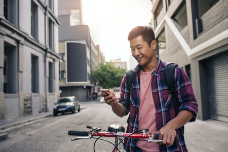 Smiling young man standing with his bike using a cellphoneの写真素材