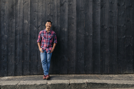 Young Asian man smiling while standing by a wall outsideの写真素材