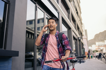 Young man walking with his bicycle talking on a cellphoneの写真素材