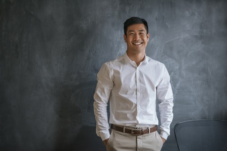 Laughing Asian businessman standing in front of a blank chalkboardの写真素材