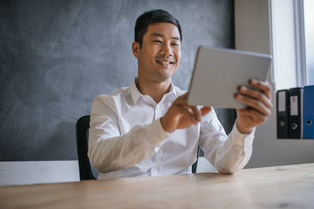 Smiling Asian businessman using a tablet at his office deskの写真素材