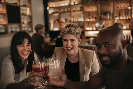 Smiling friends cheering together with drinks at a bar tableの写真素材