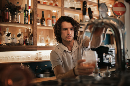 Bartender preparing drinks behind a bar counter at nightの写真素材
