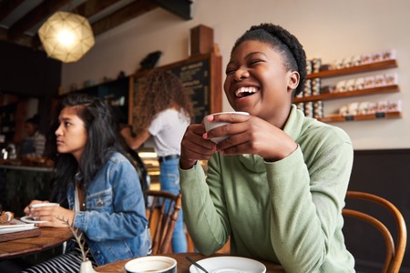 Young woman laughing over coffee with friends in a cafeの写真素材