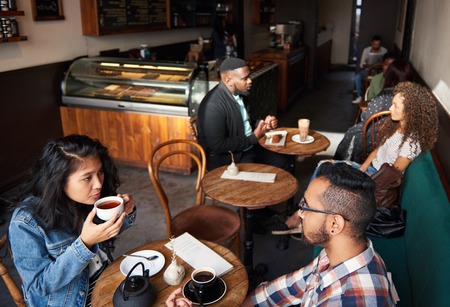 Multiethnic crowd sitting at tables in a trendy cafeの写真素材