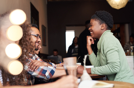 Young woman laughing while talking with friends in a cafeの写真素材