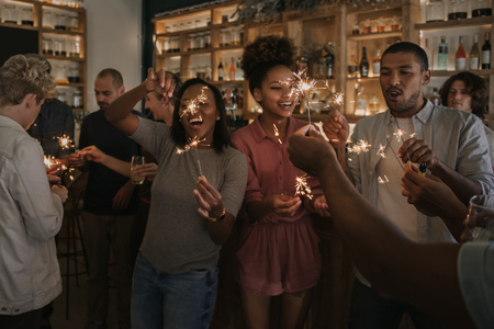 Laughing friends celebrating with sparklers in a bar at night