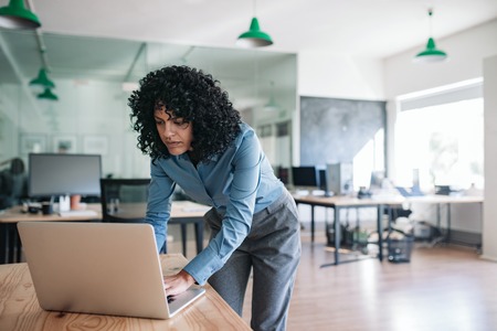 Young businesswoman standing over her office desk using a laptopの写真素材