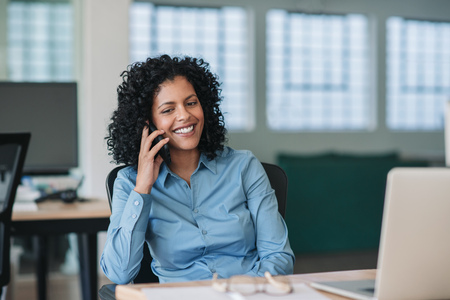 Smiling businesswoman sitting at her desk talking on a cellphoneの写真素材