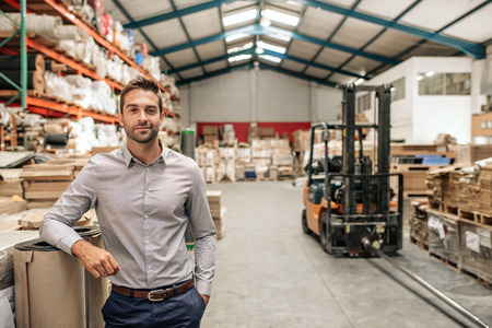 Smiling manager leaning against stock in a large warehouseの写真素材