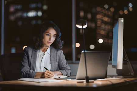 Young businesswoman writing notes in an office at nightの写真素材