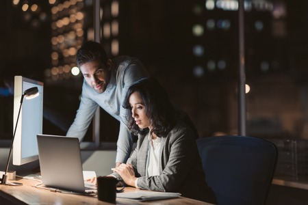 Two businesspeople working together in an office late at nightの写真素材