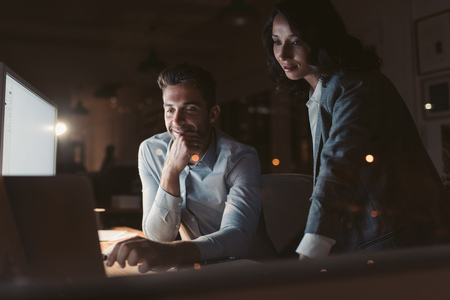 Two businesspeople working in a dark office at nightの写真素材