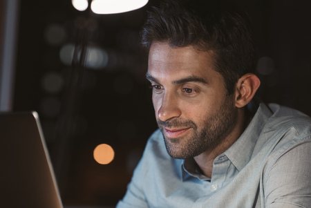 Smiling businessman working online in his office at nightの写真素材