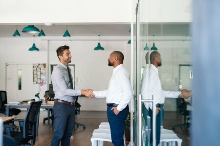 Two smiling businessmen shaking hands together after an office meeting