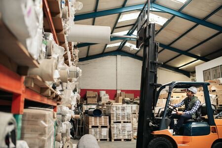 Forklift driver taking stock off shelves in a large warehouseの写真素材