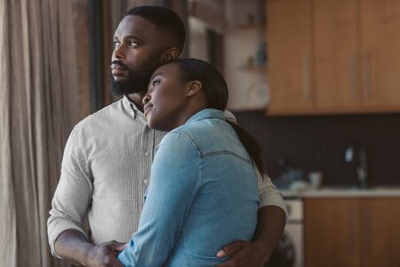African American couple hugging and looking out of their windowの写真素材