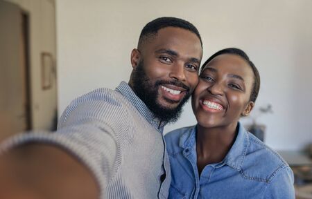 Smiling young African American couple taking selfies at homeの写真素材