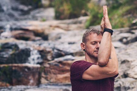Man doing the eagle pose on rocks by a waterfallの写真素材