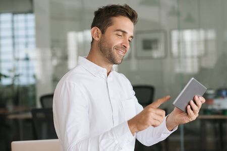 Smiling businessman standing in an office using a digital tabletの写真素材