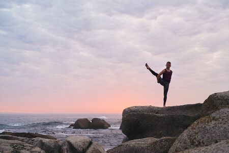 Man doing the bird of paradise pose by the oceanの写真素材