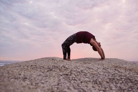 Man doing the wheel pose on some rocks at duskの写真素材