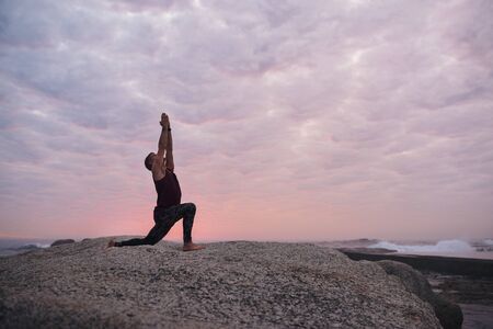 Man doing the cresent lunge pose by the oceanの写真素材