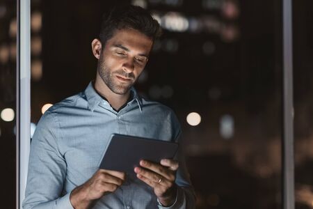 Handsome businessman using a tablet in his office at nightの写真素材