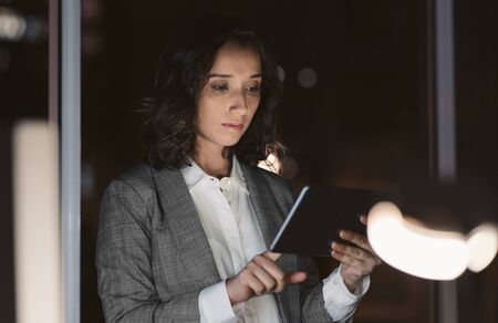 Young businesswoman using her tablet in a dark officeの写真素材