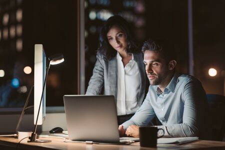 Businesspeople working together on a laptop late in the eveningの写真素材