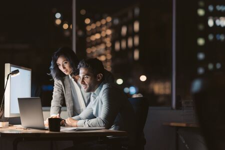 Two work colleagues using a laptop late in the eveningの写真素材