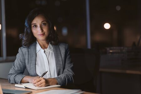 Young businesswoman smiling while working in her office at nightの写真素材
