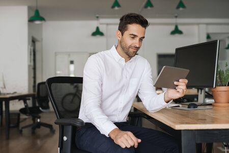 Smiling businessman working on a tablet in an officeの写真素材