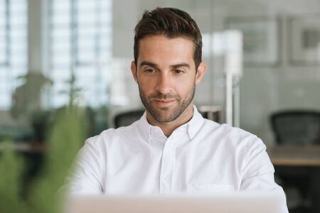 Smiling young businessman working on a laptop in his officeの写真素材