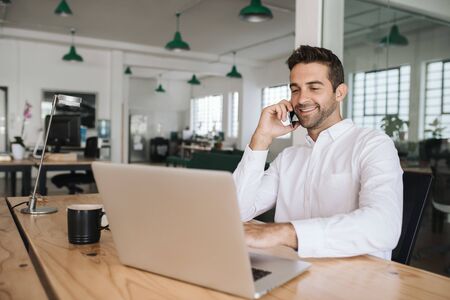 Smiling businessman sitting at his desk talking on a cellphoneの写真素材