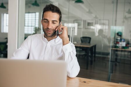 Smiling businessman talking on his cellphone at an office deskの写真素材