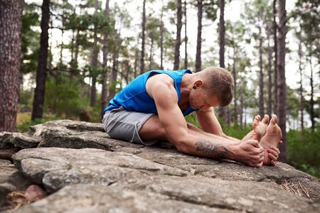 Man doing the posterior stretch pose in a forestの写真素材