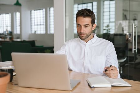 Young businessman writing down notes while working on a laptopの写真素材