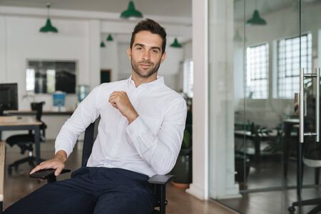 Confident young businessman sitting in a chair in an officeの写真素材